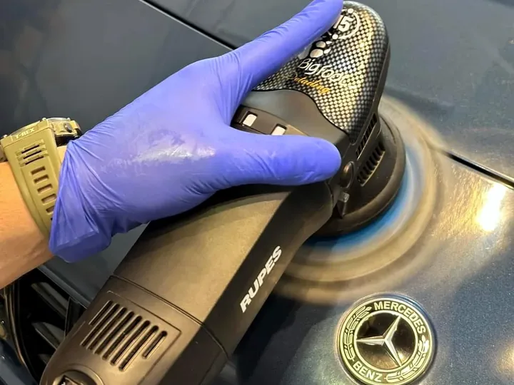 Andrzej polijst de blauwe motorkap van een Mercedes met een Rupes-machine